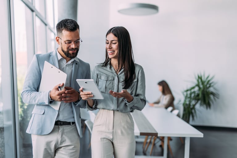 Two confident business persons talking in the workplace using a digital tablet while walking in a modern office